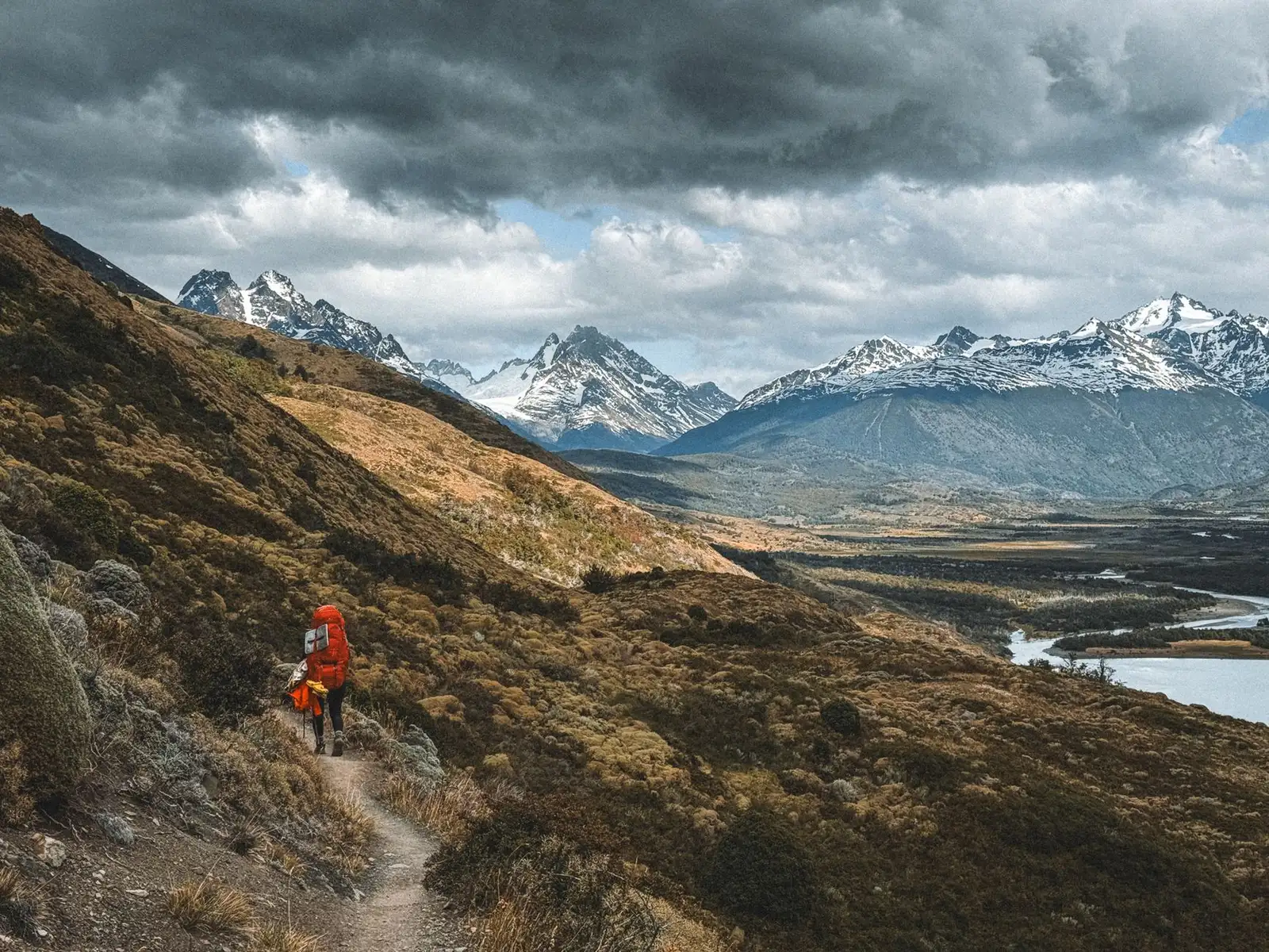 A solo hiker trekking through the stunning mountains of Magallanes, Chile, with dramatic skies overhead.