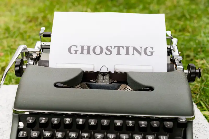 A vintage typewriter displaying the word 'Ghosting' on a white paper, set outdoors on grass.